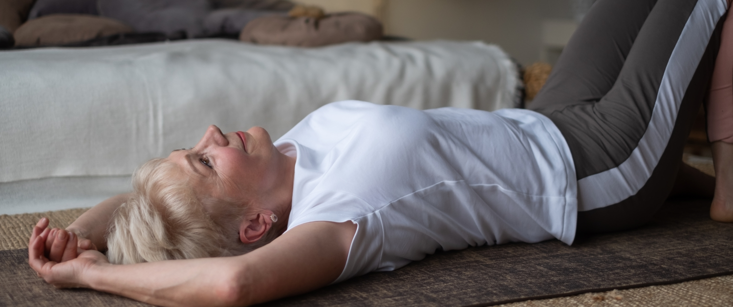 Senior sporty woman practicing yoga, lying on floor resting after yoga